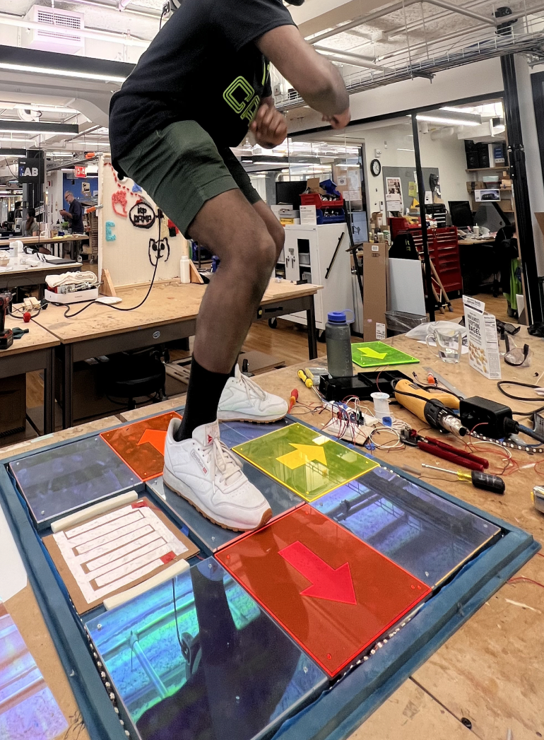 A person mid-jump on a DIY interactive light-up dance mat in a workshop